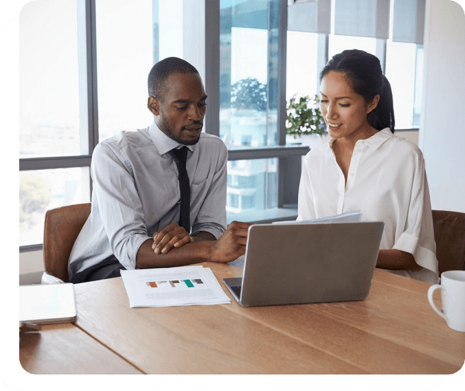 Two people sitting at a table looking at a laptop.